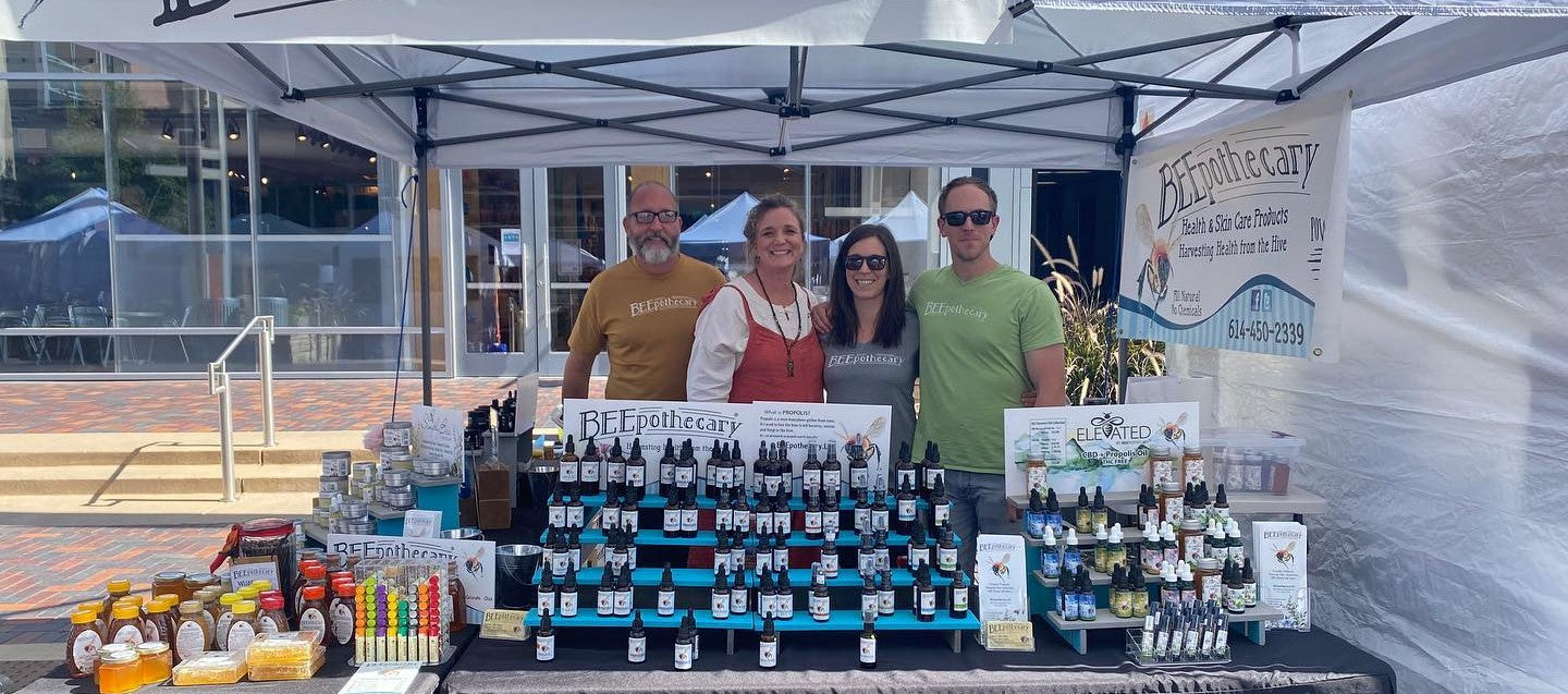 Pete and Laurie standing next to friends within their BEEpothecary event tent.