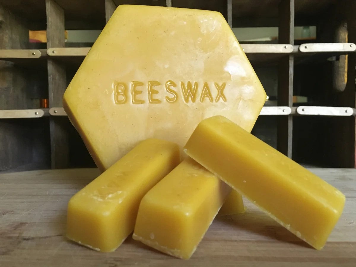 BEEpothecary bulk beeswax displaying 1 lb hexagon shape in the background with 1 oz ingots in the foreground in yellow waxlike consistency.