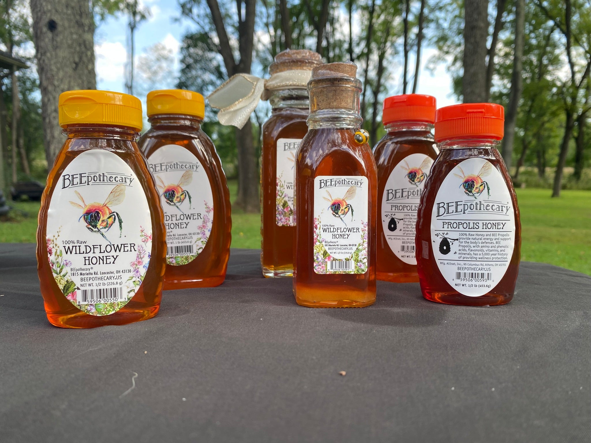 BEEpothecary honey products on a table outside. Honey is golden orange color.