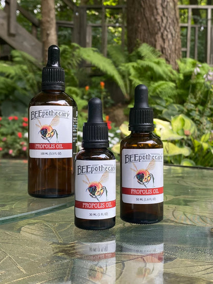Propolis oil products sitting on a table outdoors with green plants behind them.